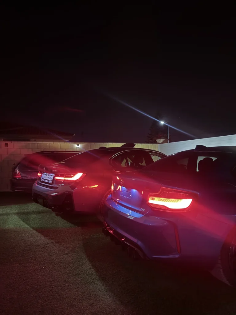 BMW M2 azul junto a otro BMW de noche con los pilotos encendidos