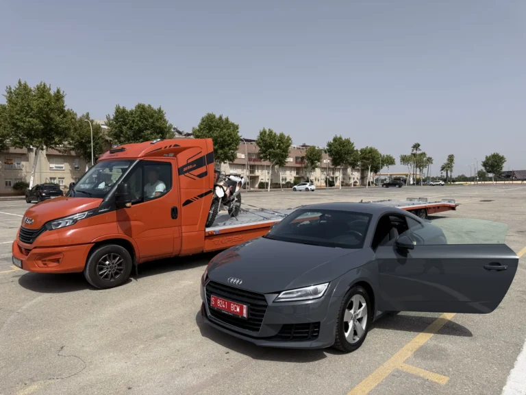 Audi TT gris recién descargado junto a un camión portacoches naranja