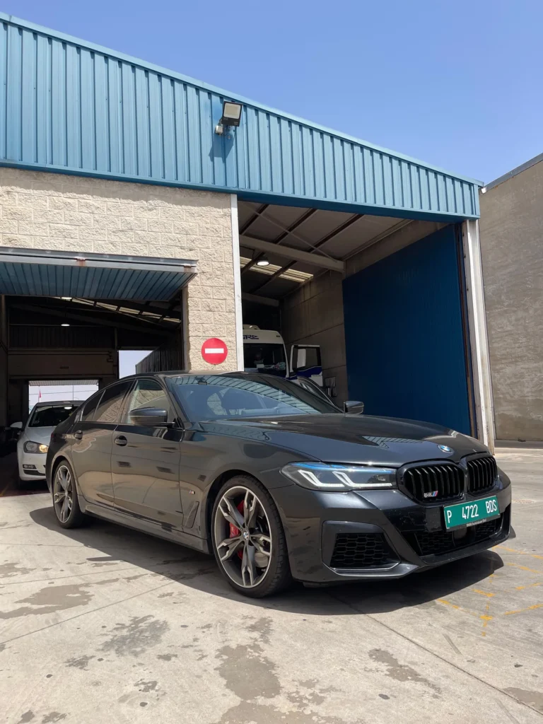 BMW Serie 5 M Sport gris aparcado frente a un taller con matrícula verde de exportación